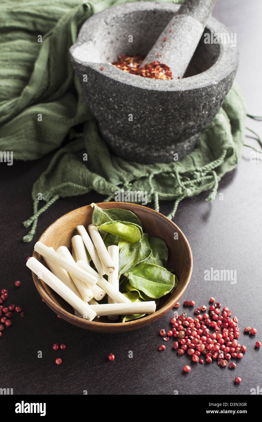 Kaffir lime leaves, lemon grass, pink peppercorns and a mortar and pestle with crushed pepper. Stock Photo
