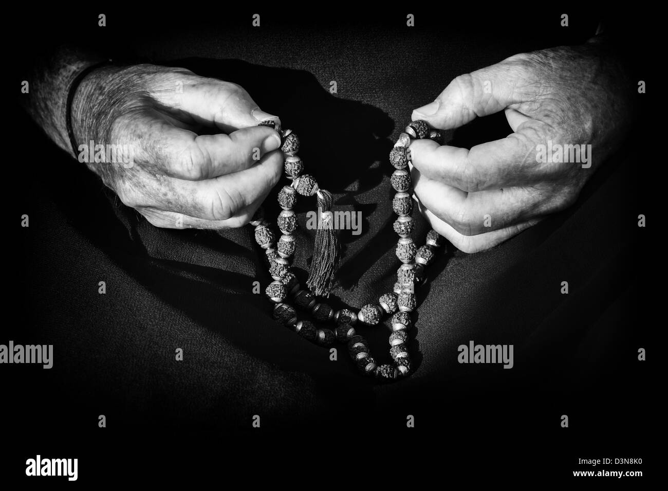 Old mans hands holding Indian Rudraksha / Japa Mala prayer beads. Monochrome Stock Photo