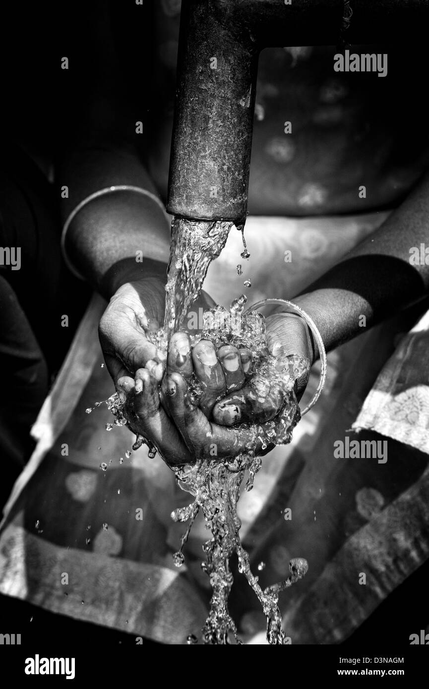 Water from a hand pump in a rural indian village pouring into an Indian girls hands. Andhra Pradesh, India. Monochrome Stock Photo