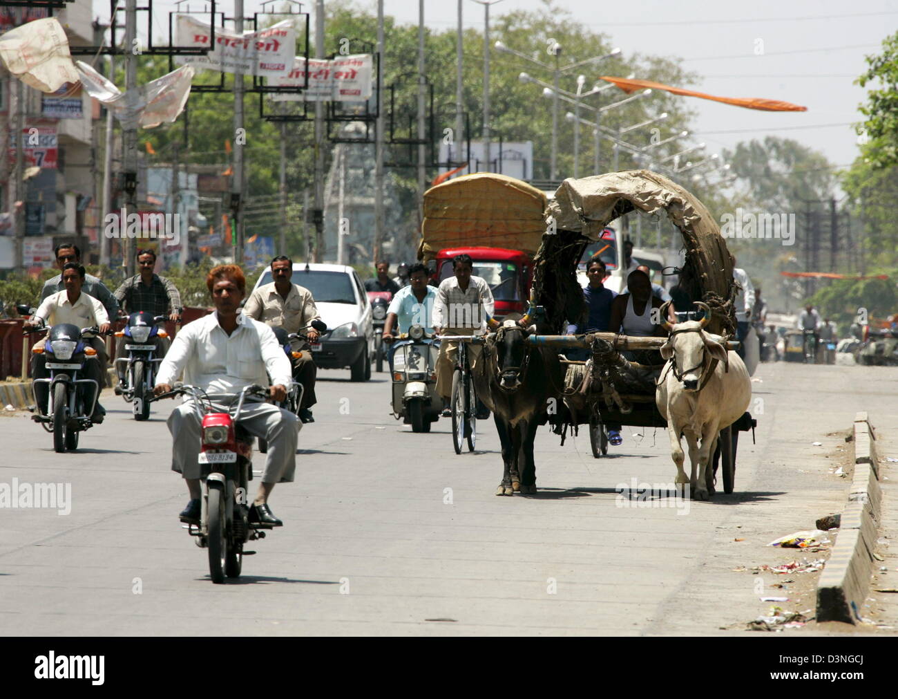 The photo shows an archaic seeming vehicle pulled by an ox between modern scooters and cars on a road in Indore, India, 28 April 2006. Indore lies in the federal state of Madhya Pradesh and counts 1.692.400 million inhabitants. It is an industrial city with cotton, metall, furniture and chemical industries, a cultural centre with a university, theatres, museums, cinemas and a scien Stock Photo