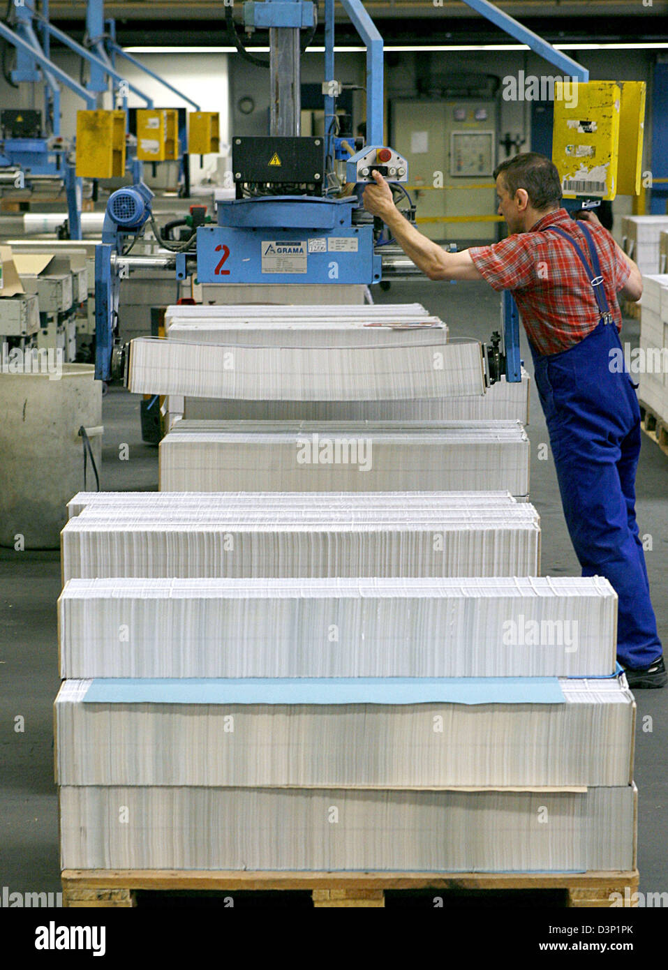 A worker puts packed printed sheets into a glue binding machine in the Prinovis printing plant in Nuremberg, Germany, 27 June 2006. Prinovis is a joint-venture of publishing companies Bertelsmann, Gruner&Jahr and Springer and one of Europe's biggest rotogravure printing companies. Photo: Daniel Karmann Stock Photo