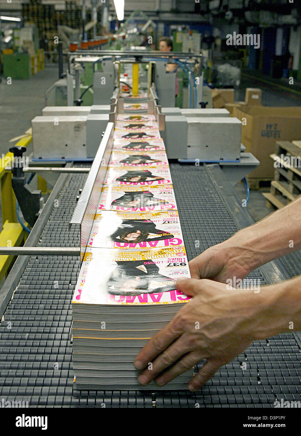 A worker stacks magazines onto a conveyor belt in the printing plant Prinovis in Nuremberg, Germany, 27 June 2006. Prinovis is a joint-venture of publishing companies Bertelsmann, Gruner&Jahr and Springer and one of Europe's biggest rotogravure printing companies. Photo: Daniel Karmann Stock Photo