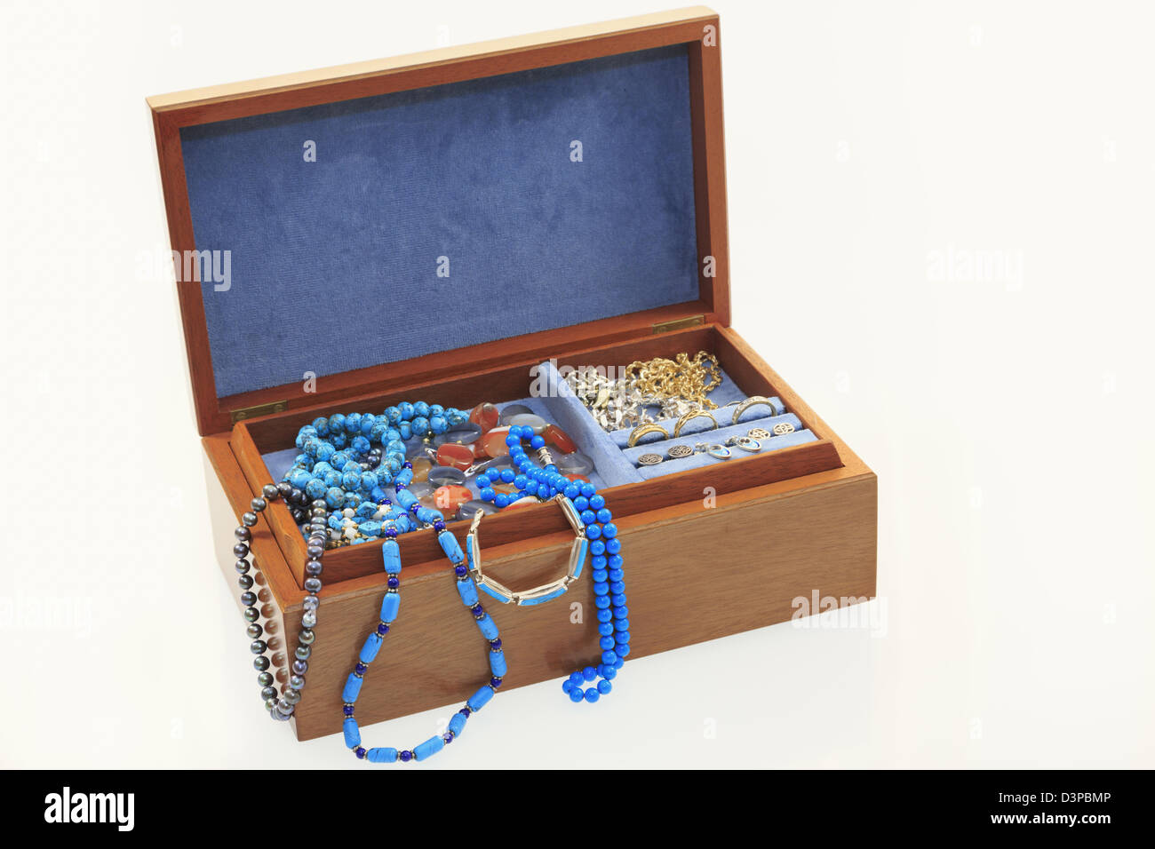 Blue velvet lined wooden jewellery box with lid open containing jewels and trinkets isolated on a plain white background. Stock Photo