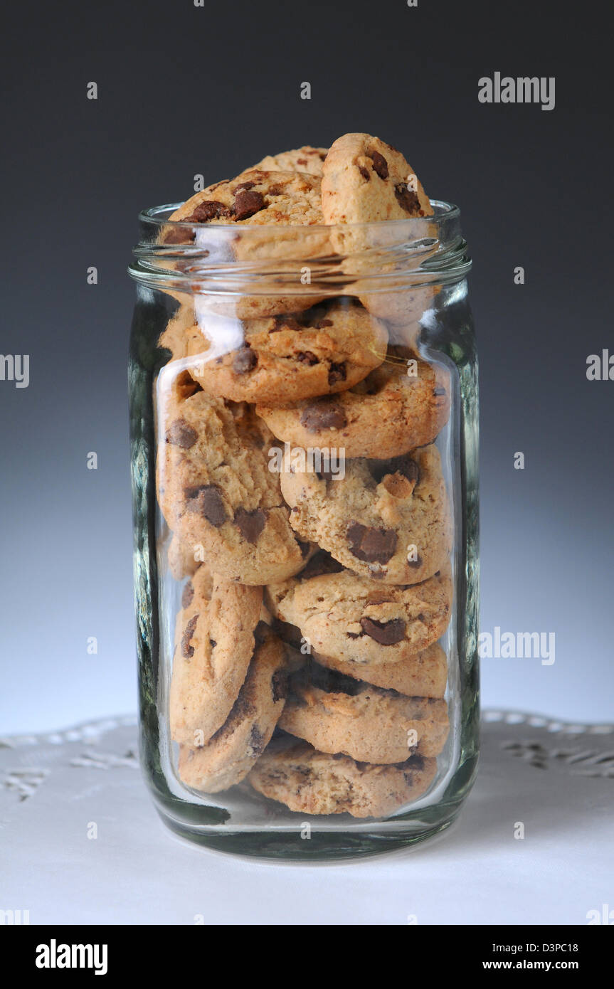 Closeup of a glass jar full of chocolate chip cookies. Vertical format on a light to dark gray background. Stock Photo
