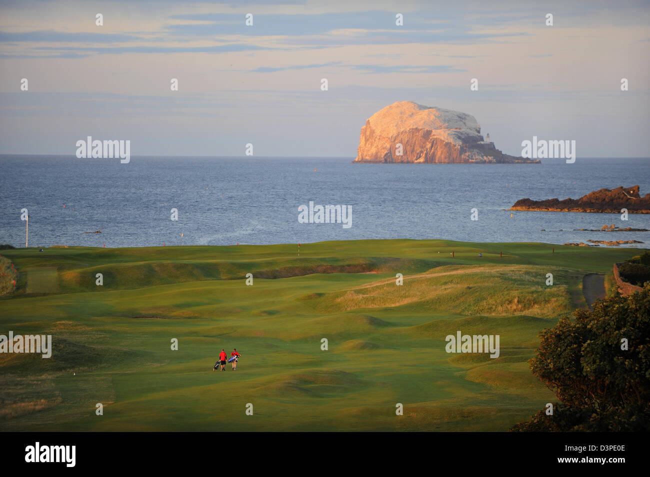 Two golfers walk up the fairway on North Berwick Golf Club as the sun sets over Bass Rock in the Firth of Forth, Scotland. Stock Photo