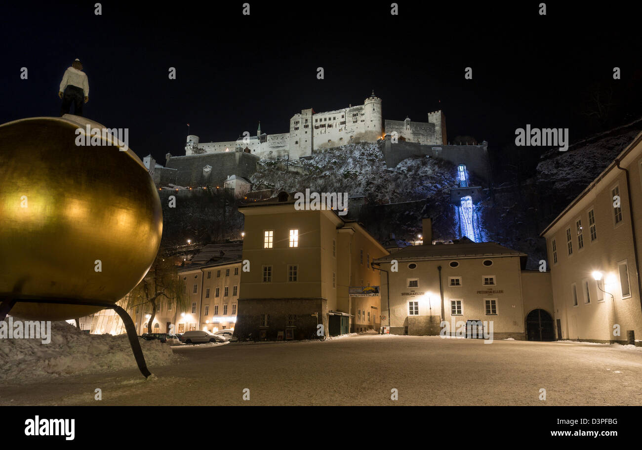Man, Sphere and Salzburg Fortress in the snow. A golden globe topped with snow and a figure staring out at the castle above. Stock Photo