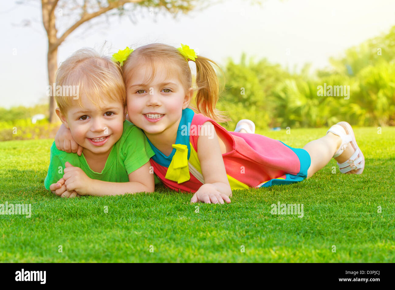 Picture of cute little girl with pretty boy lying down on green grass in park, cheerful children resting on the field Stock Photo
