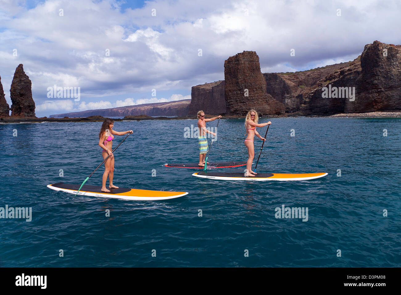 Three young people on stand-up paddle boards at Needles off the island of Lanai, Hawaii. All three are model released. Stock Photo