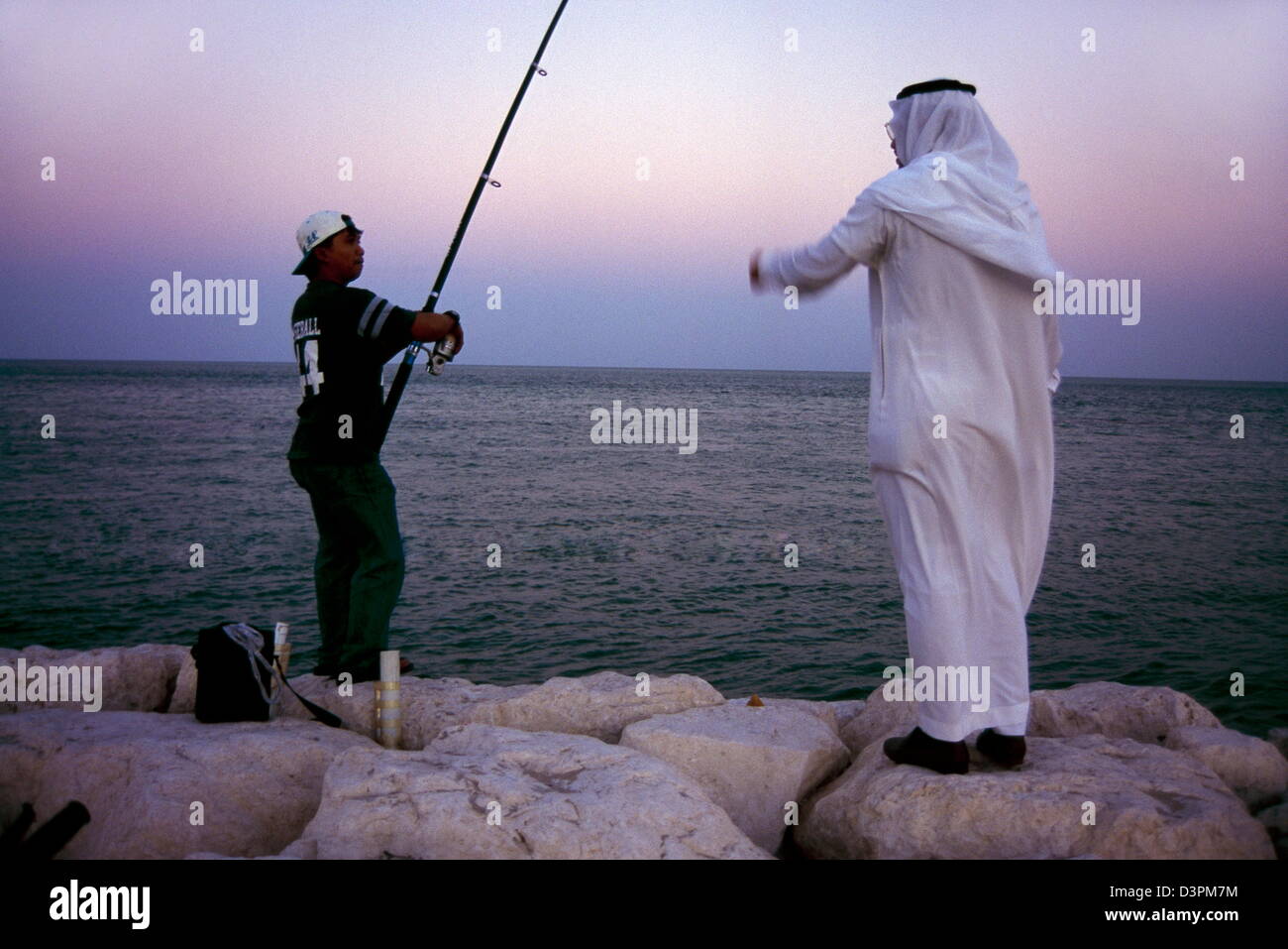 A Saudi chats with a third country national while fishing on his leisure time as the sunsets over the Persian Gulf in al khobar. Stock Photo