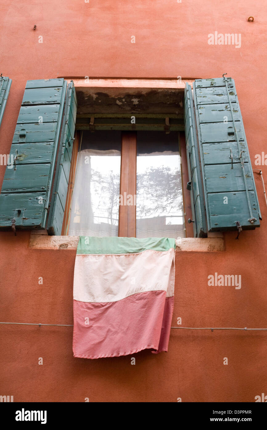 Terracotta Painted Wall with Shutters and the Italian Flag Hanging from it Stock Photo
