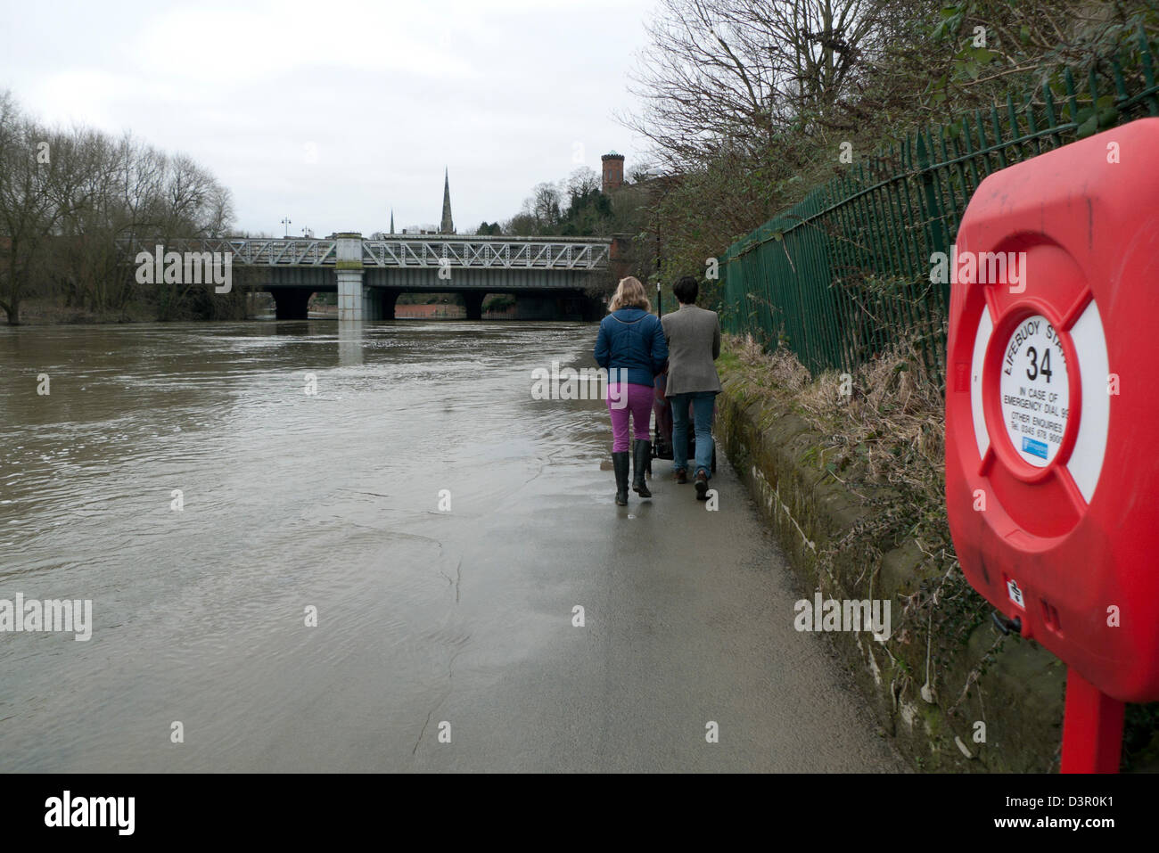 Rear view of couple with a pram struggling to walk along a pavement on the flooded River Severn Shrewsbury in Shropshire England UK  KATHY DEWITT Stock Photo