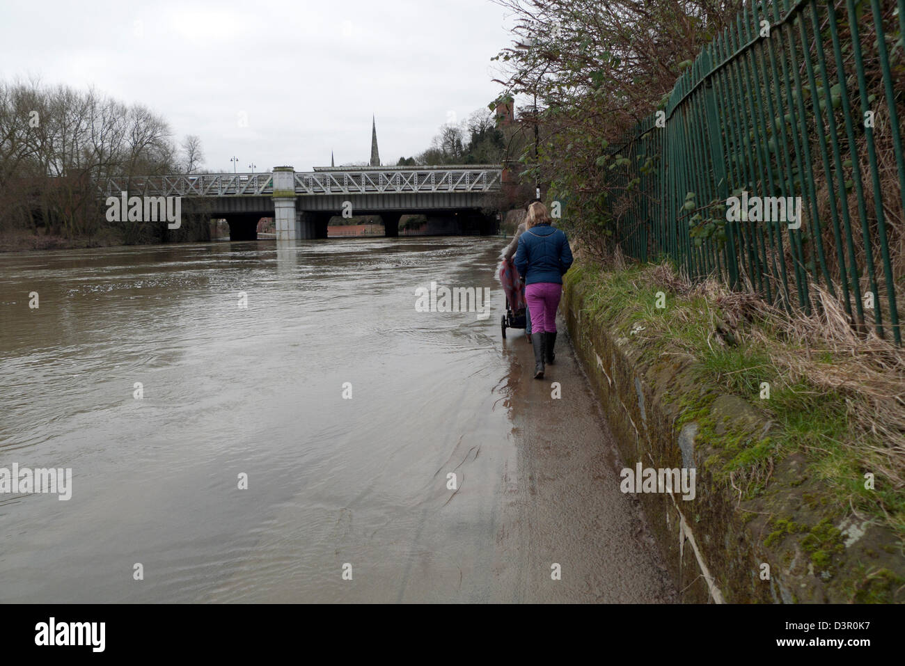 A couple with a pram struggling to walk along a pavement on the flooded River Severn Shrewsbury Shropshire England UK Stock Photo