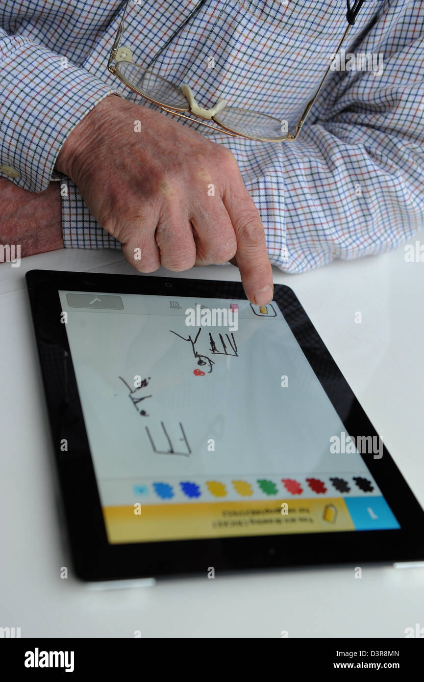 75 year old Grandfather playing Draw Something app against his grandchild on the Ipad. Stock Photo