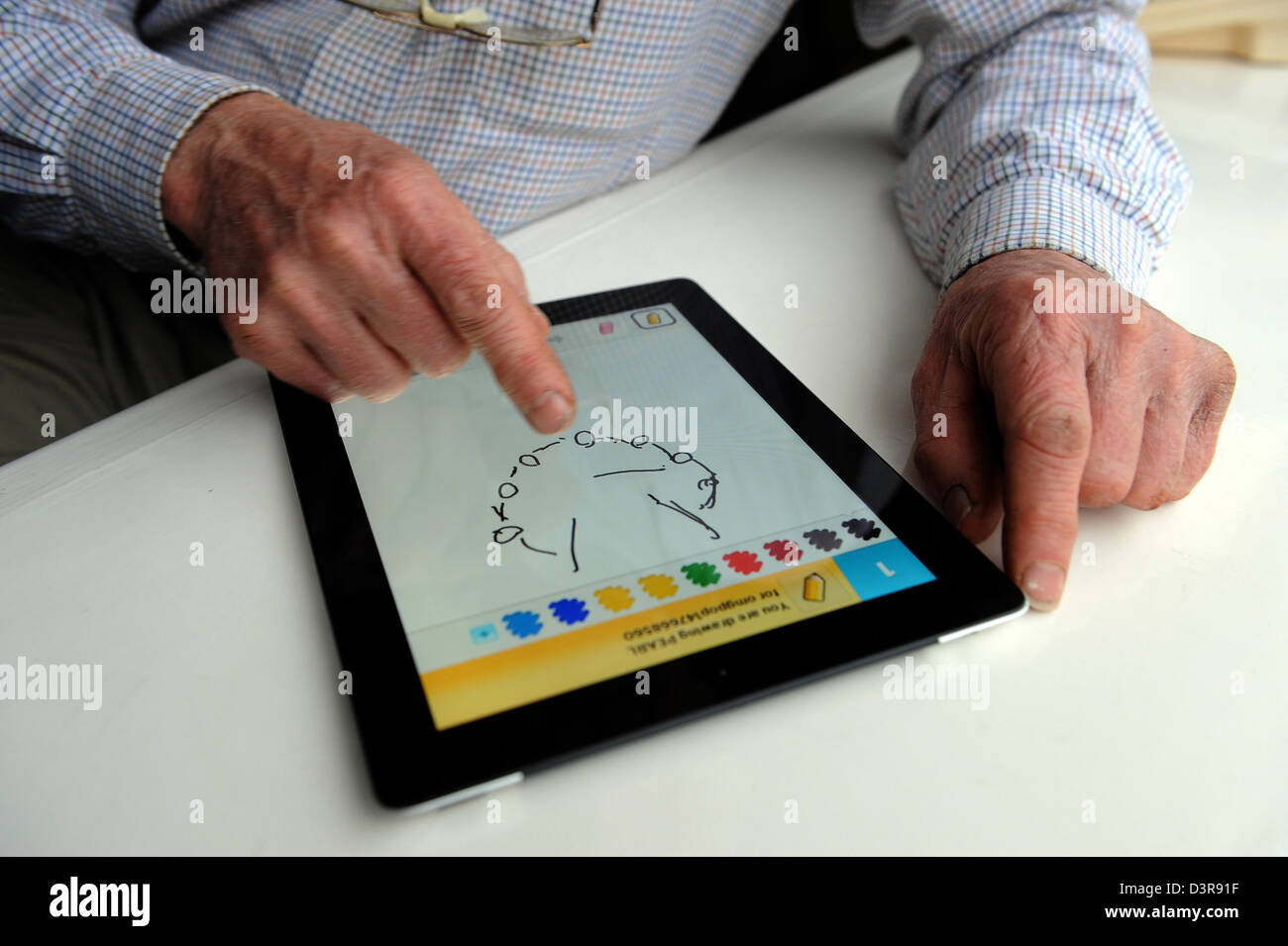 75 year old Grandfather playing Draw Something app against his grandchild on the Ipad. Stock Photo