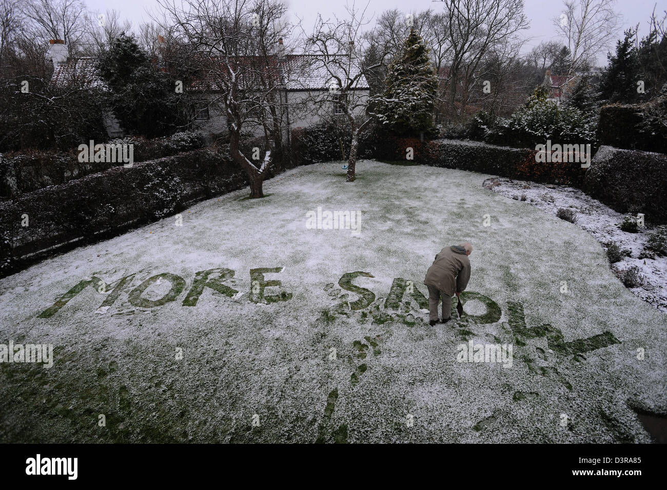 Elderly grandfather writing a humorous message MORE SNOW in snow in the garden Stock Photo