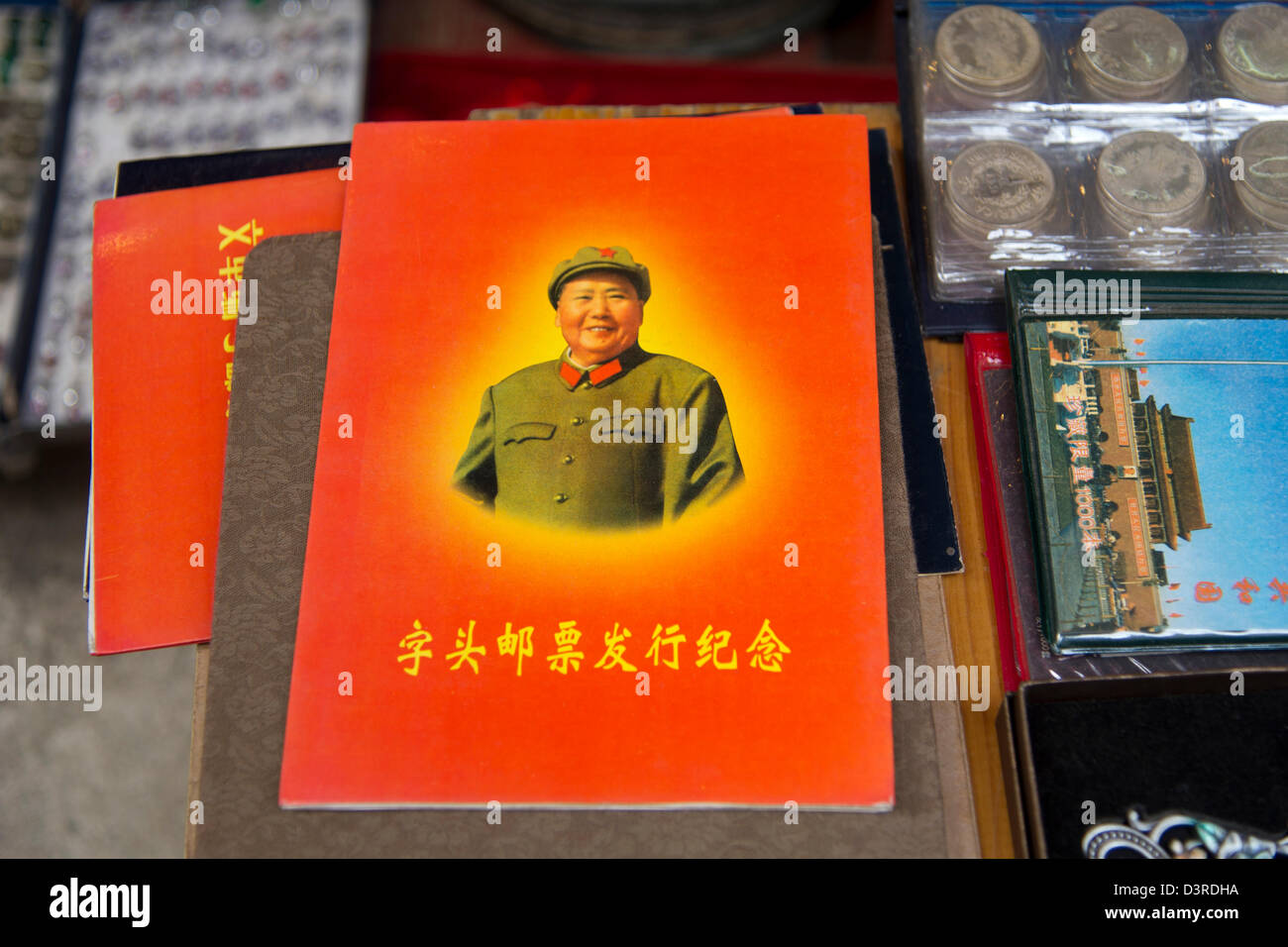 A red paperback book bearing a photo of Chairman Mao sits on a table amongst antiques at an antique market in Hong Kong. Stock Photo