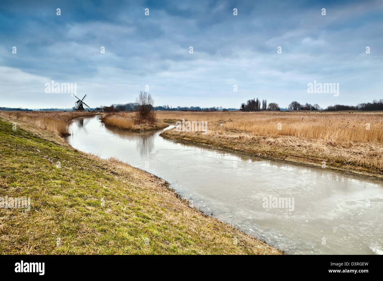 frozen river and dutch windmill in clouded morning Stock Photo