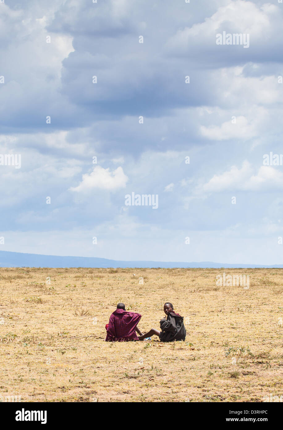 Masai children sit on the savannah looking out into the vast distance of the Serengeti plain. Tanzania Stock Photo