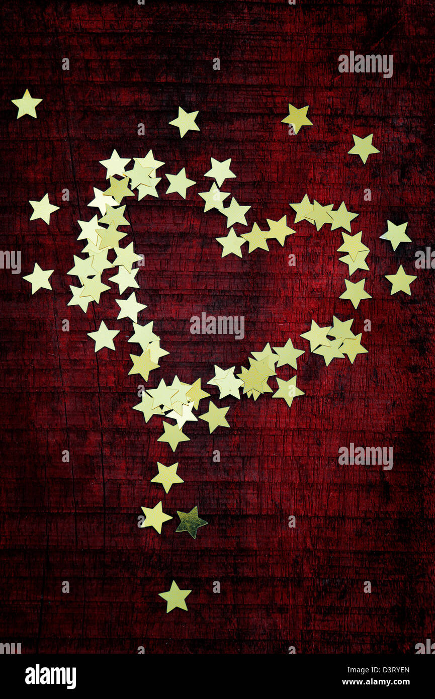 Shiny gold stars in a heart shape on a dark red wood background Stock Photo