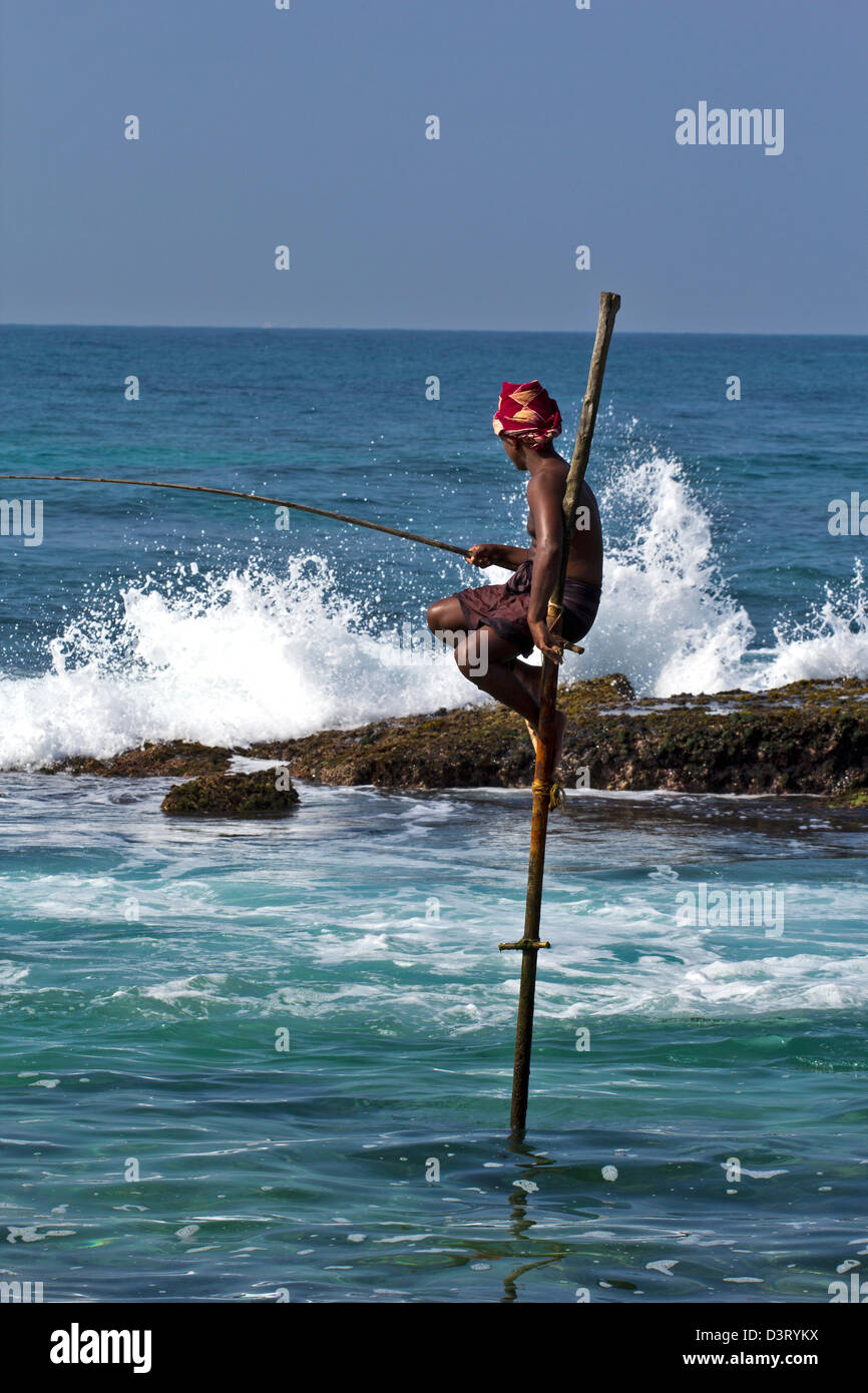 STILT FISHERMAN OF SRI LANKA FISHING NEAR ROCKS WITH CRASHING WAVES AND