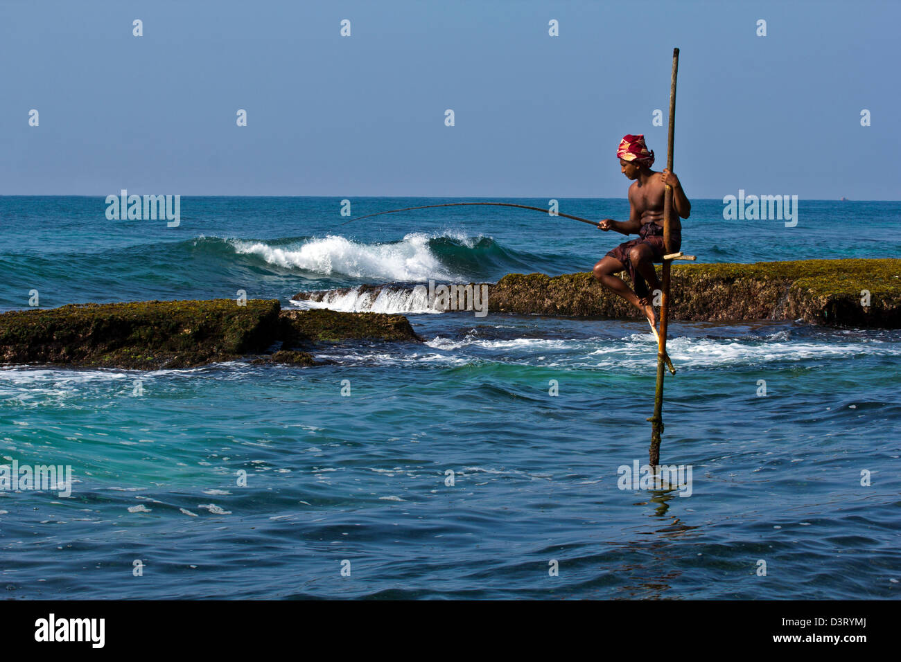STILT FISHERMAN OF SRI LANKA FISHING BETWEEN THE ROCKS Stock Photo