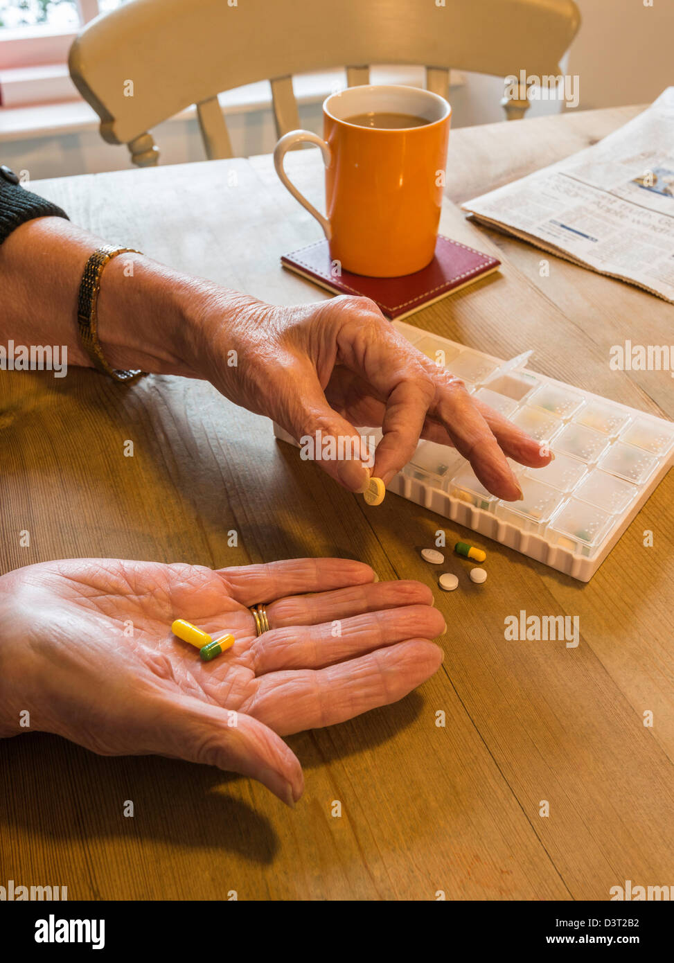 WOMAN AT TABLE WITH PILLBOX TAKING MEDICINE SORTING PILLS UK Stock Photo