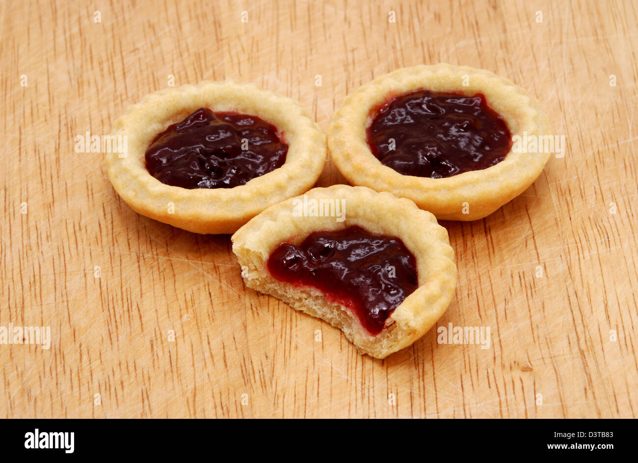 Three yummy jam tarts, one with a bite taken from it, on a wooden table Stock Photo