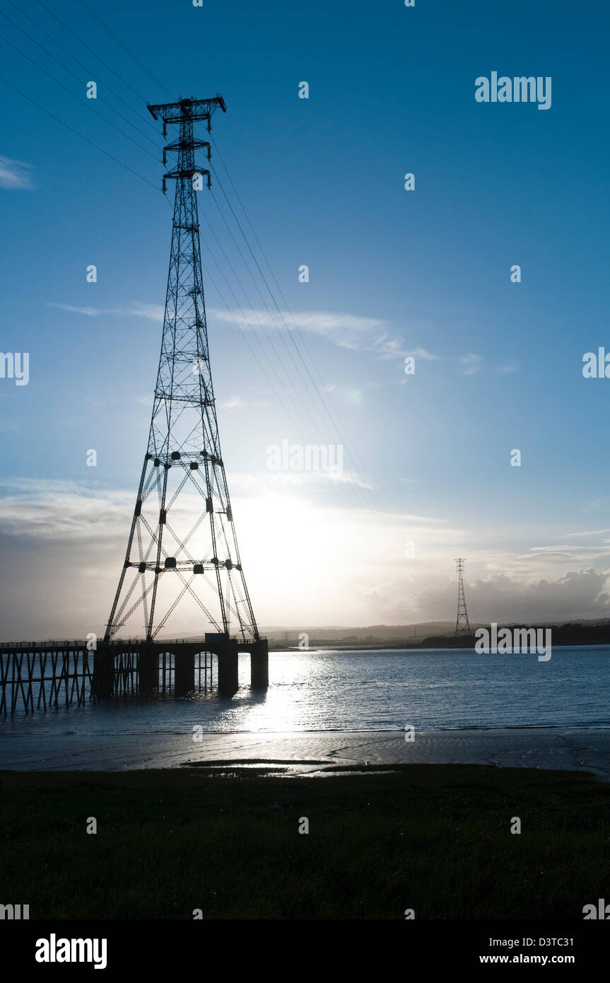 Tall power pylons at Aust carrying high energy electric lines across the river Severn with a low sun reflecting off the water. Stock Photo