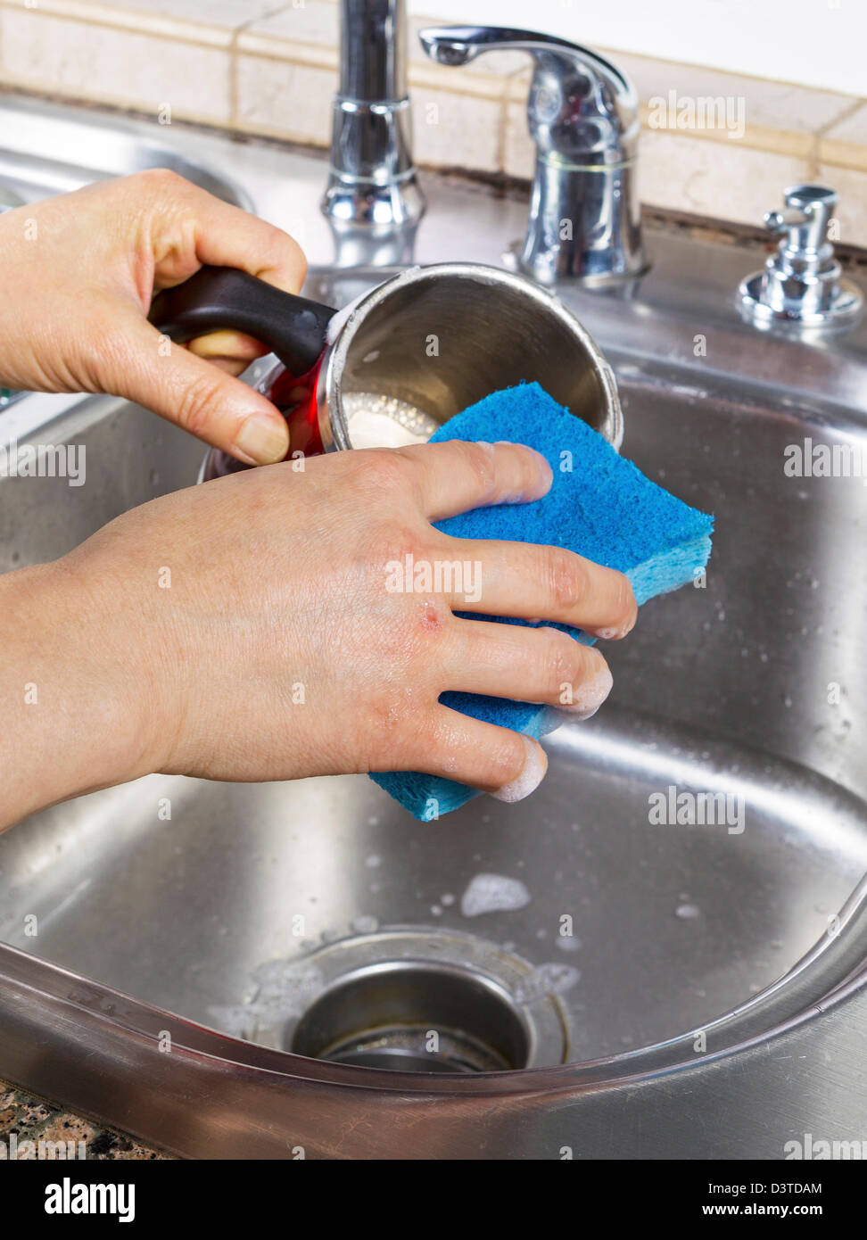 Vertical photo of female hands cleaning a coffee mug with soapy water
