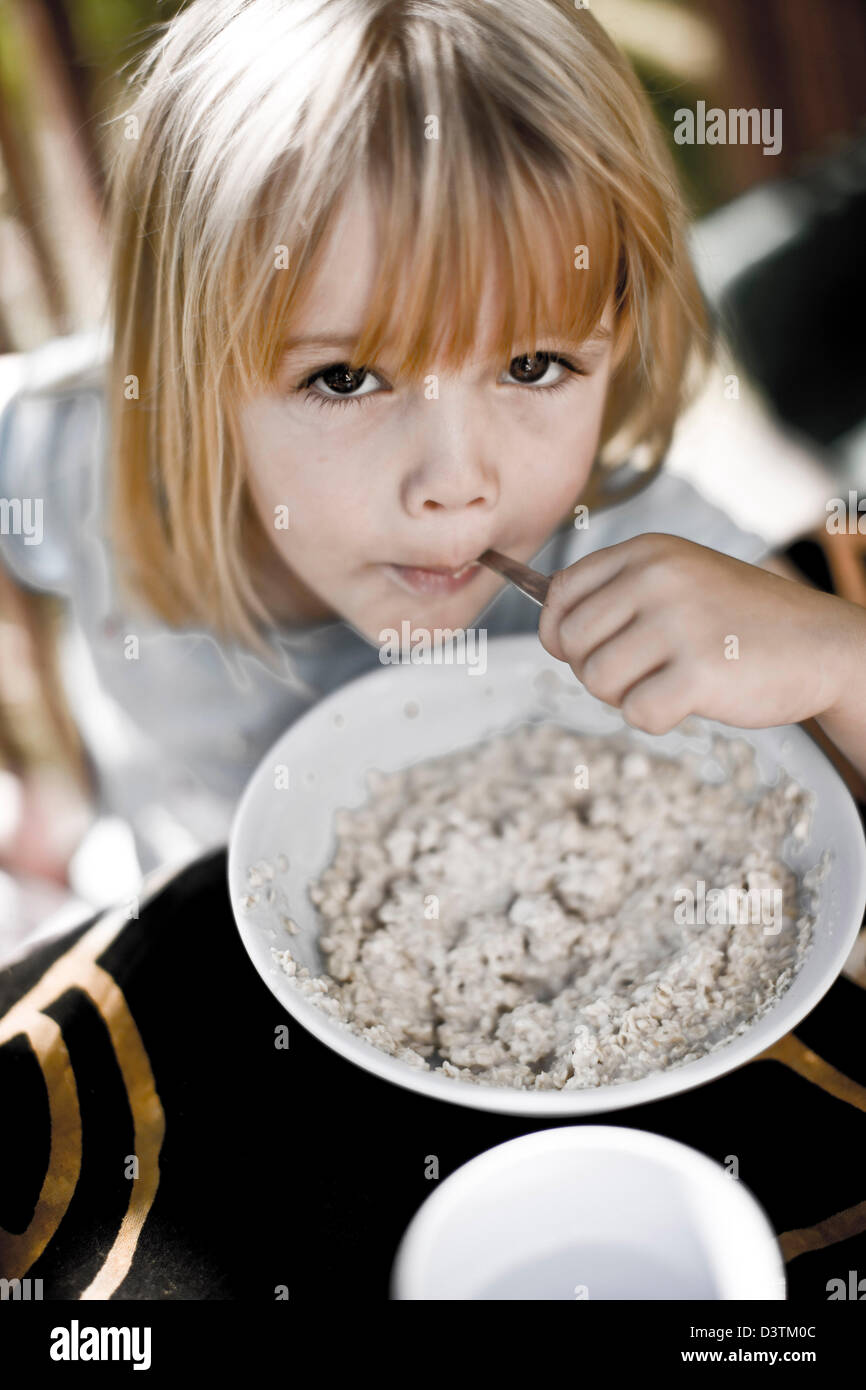 Girl eating porridge with spoon, breakfast in Pau, France Stock Photo