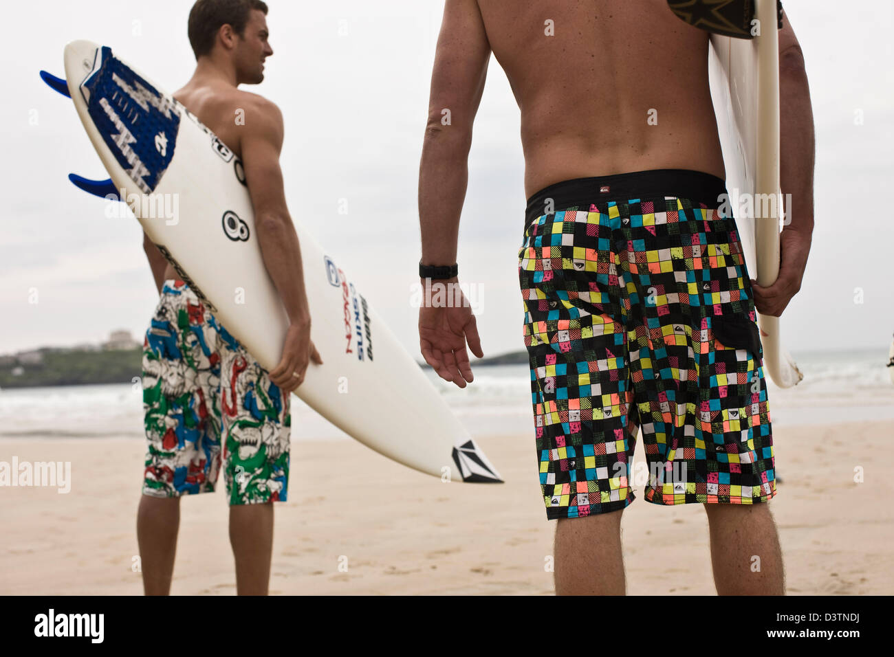 Surfers standing with boards, looking out to sea, St Agnes, Cornwall, UK Stock Photo