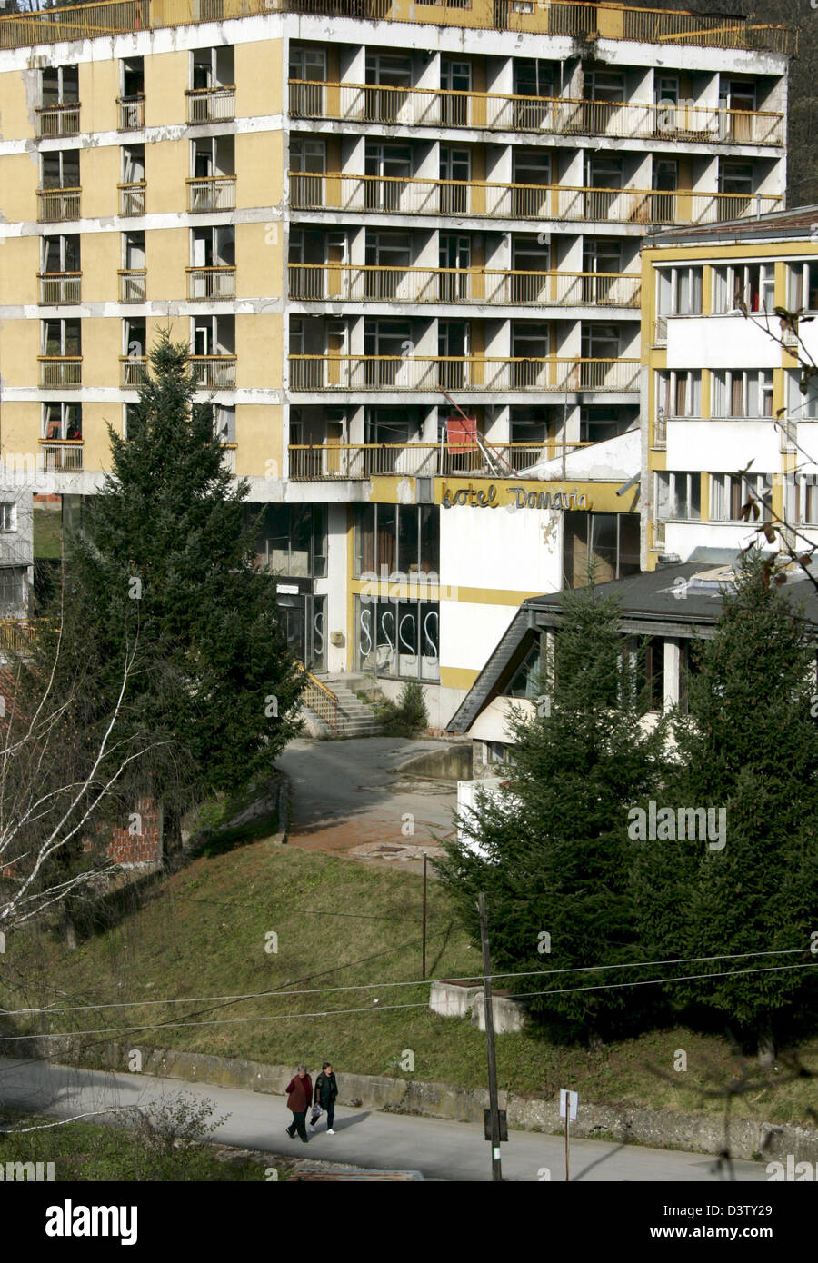 Two people pass by a house of Srebrenica, Bosnia and Herzegovina, 15 November 2006. Srebrenica is located at the border to Serbia. The city's number of inhabitants went down to 21,000, mostly Serbs and Serbian refugees from the Bosnian-Croatian Federation. The city set the sad scene for the massacre in July 1995, when Bosnian Serbs under the commando of General Ratko Mladic invaded Stock Photo