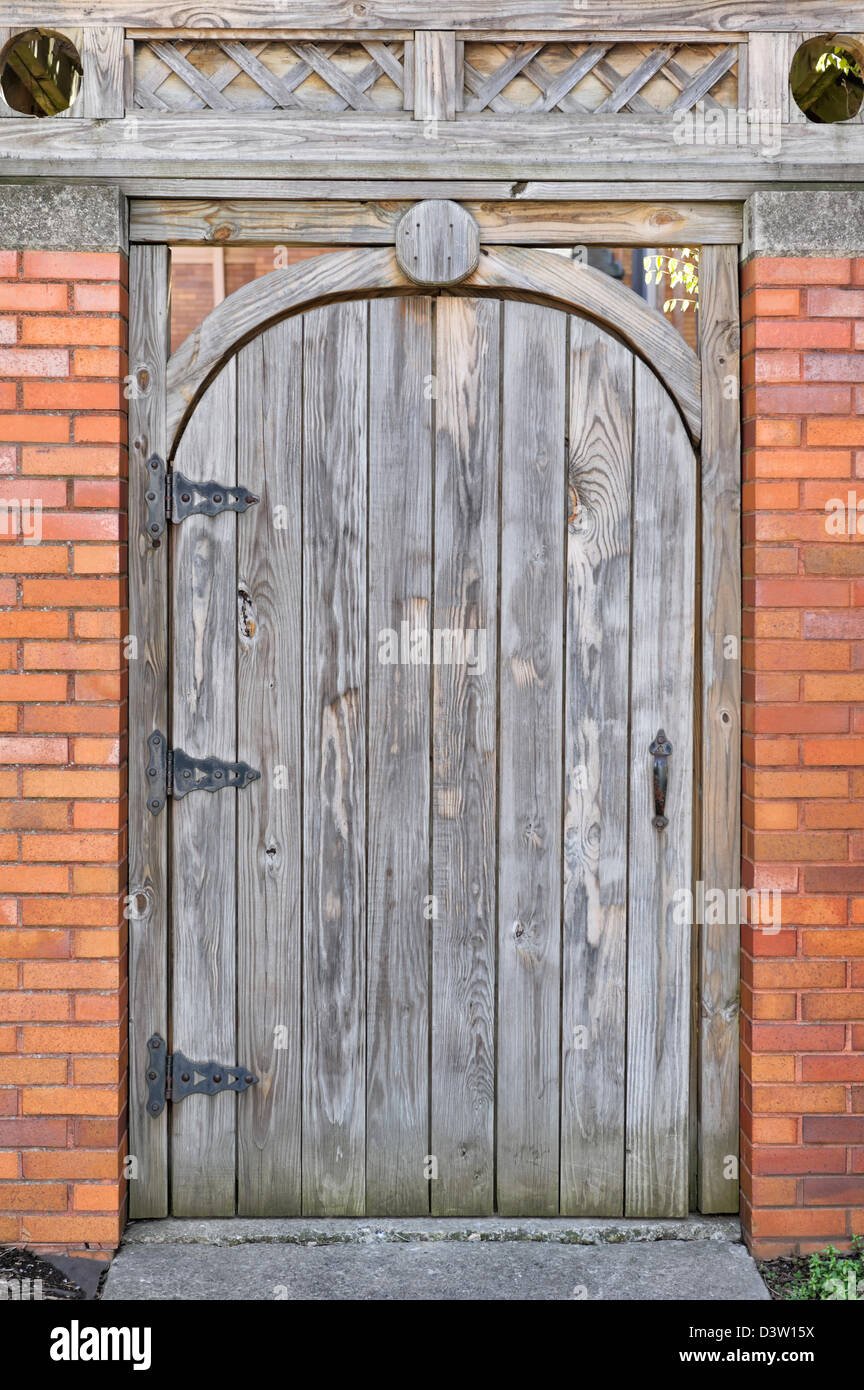 Wooden door with rounded top in brick wall close up, a garden gate shut and locked. Stock Photo