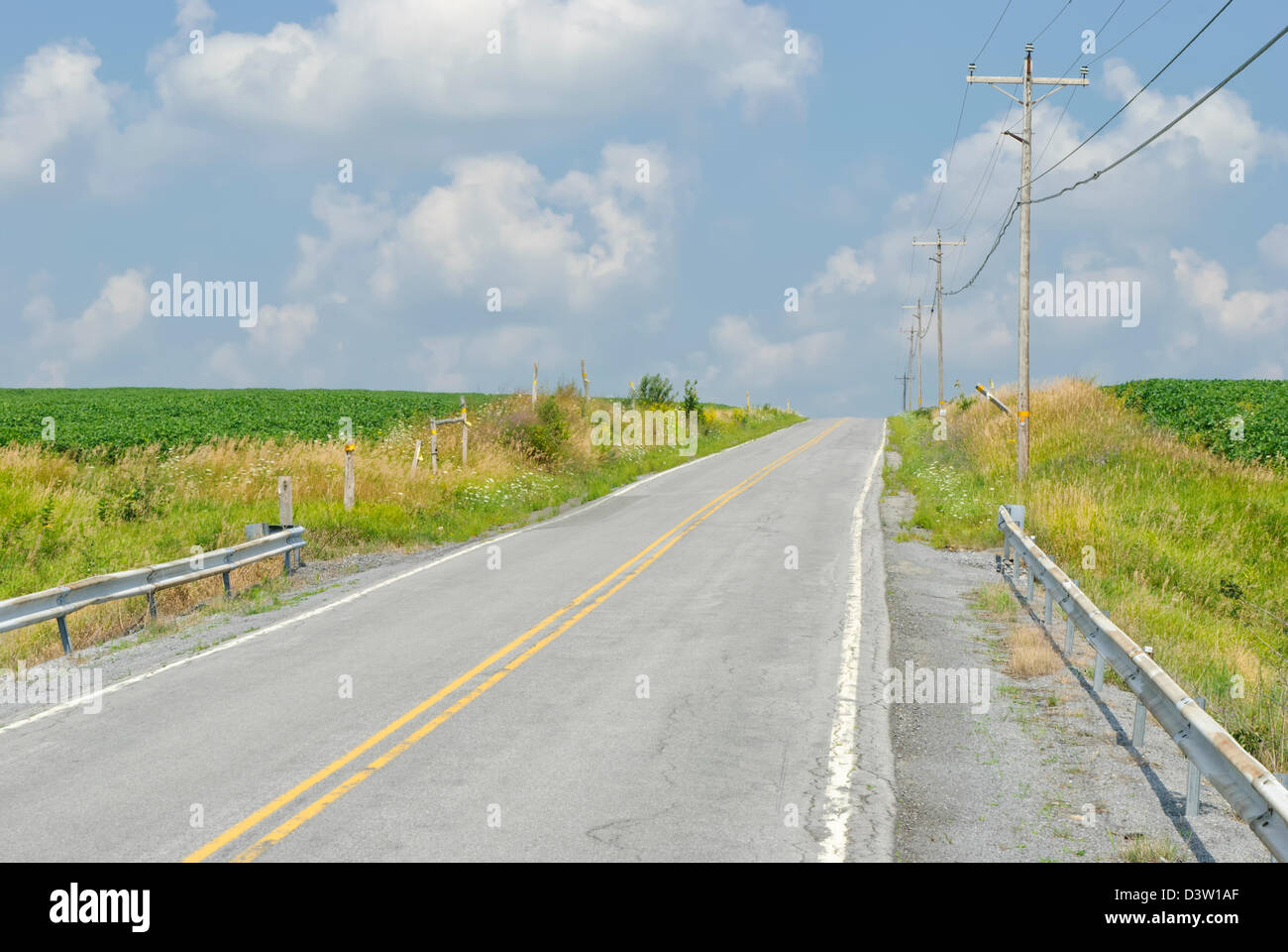 Country road heading over a hill under sunny blue skies with white clouds, a two lane summer highway in rural Pennsylvania, PA, Stock Photo
