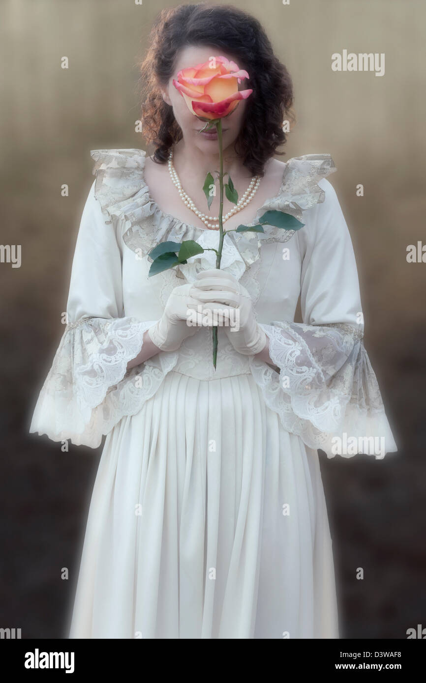 a lady in a victorian dress is holding a rose in front of her face Stock Photo