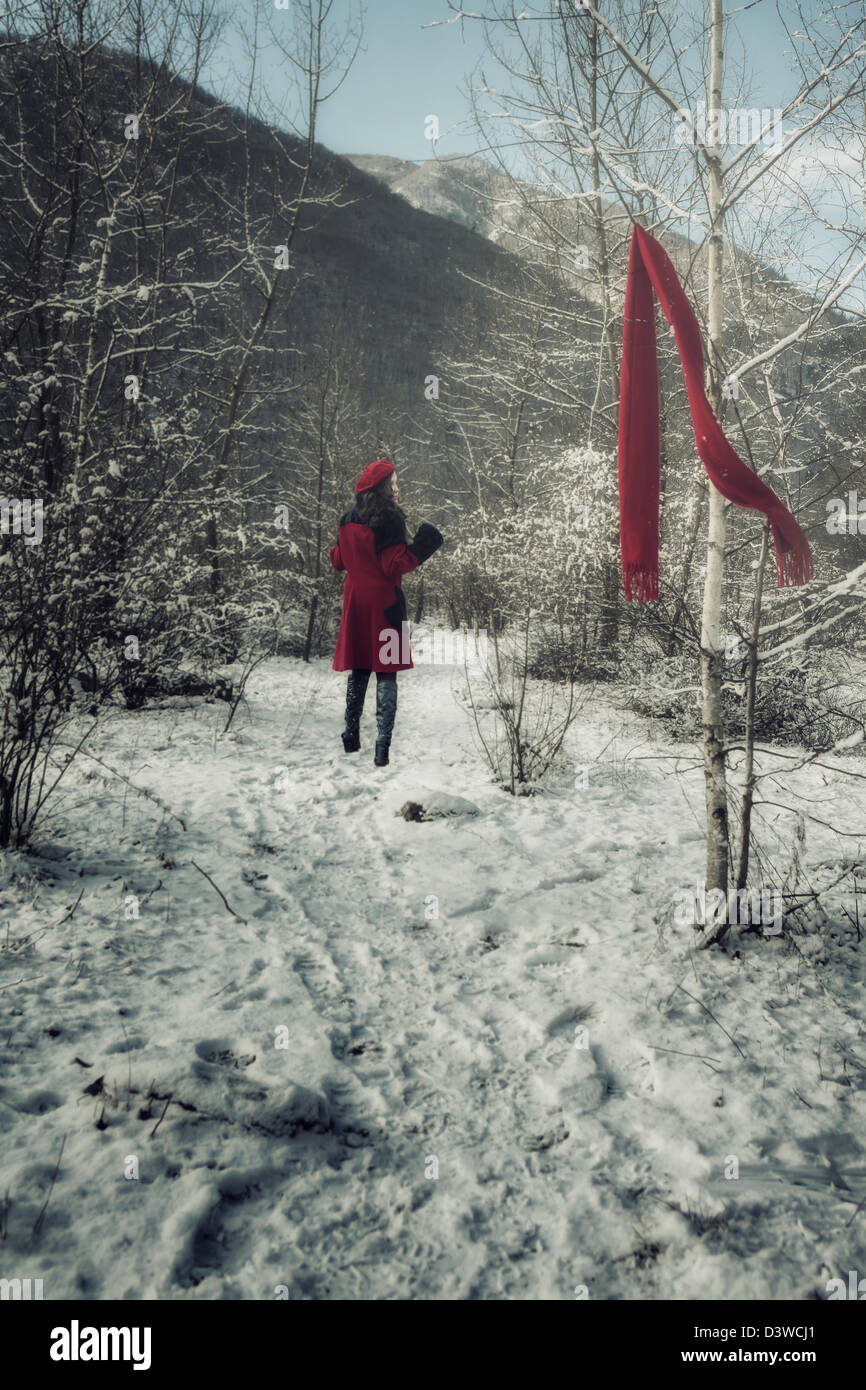 a young woman in a red coat is running through a wintery forest and lost her red shawl Stock Photo