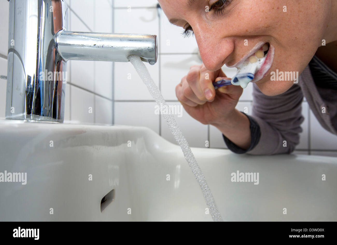 Woman is brushing her teeth, while water is still running from the tap. Symbol image for water wastage. Stock Photo