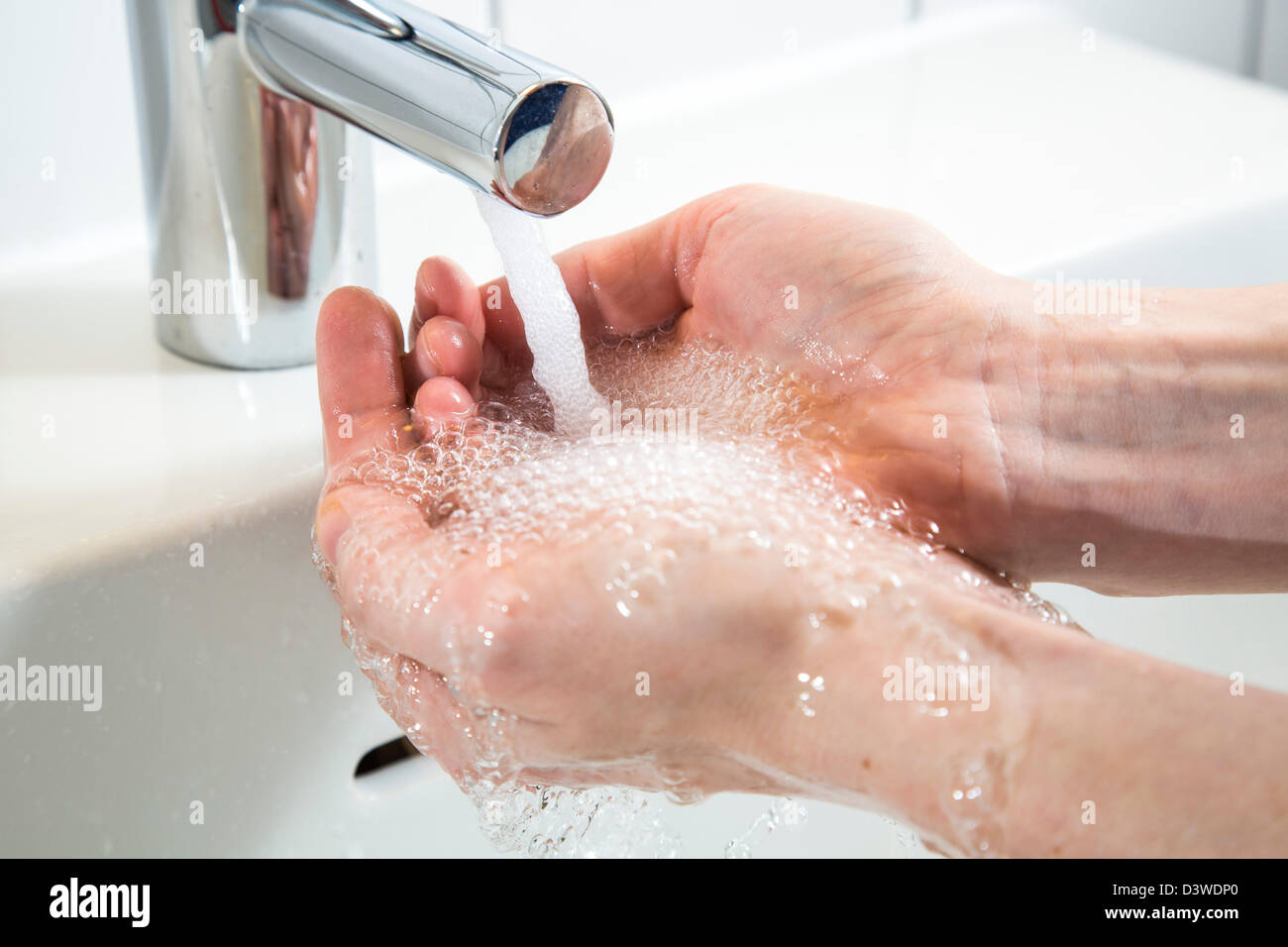 Person is washing her hands under running water from a tap in a bathroom. Symbol image for water wastage. Stock Photo
