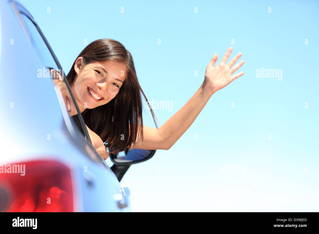 Beautiful smiling young mixed race Chinese Asian / Caucasian woman popping head out the window waving at camera Stock Photo