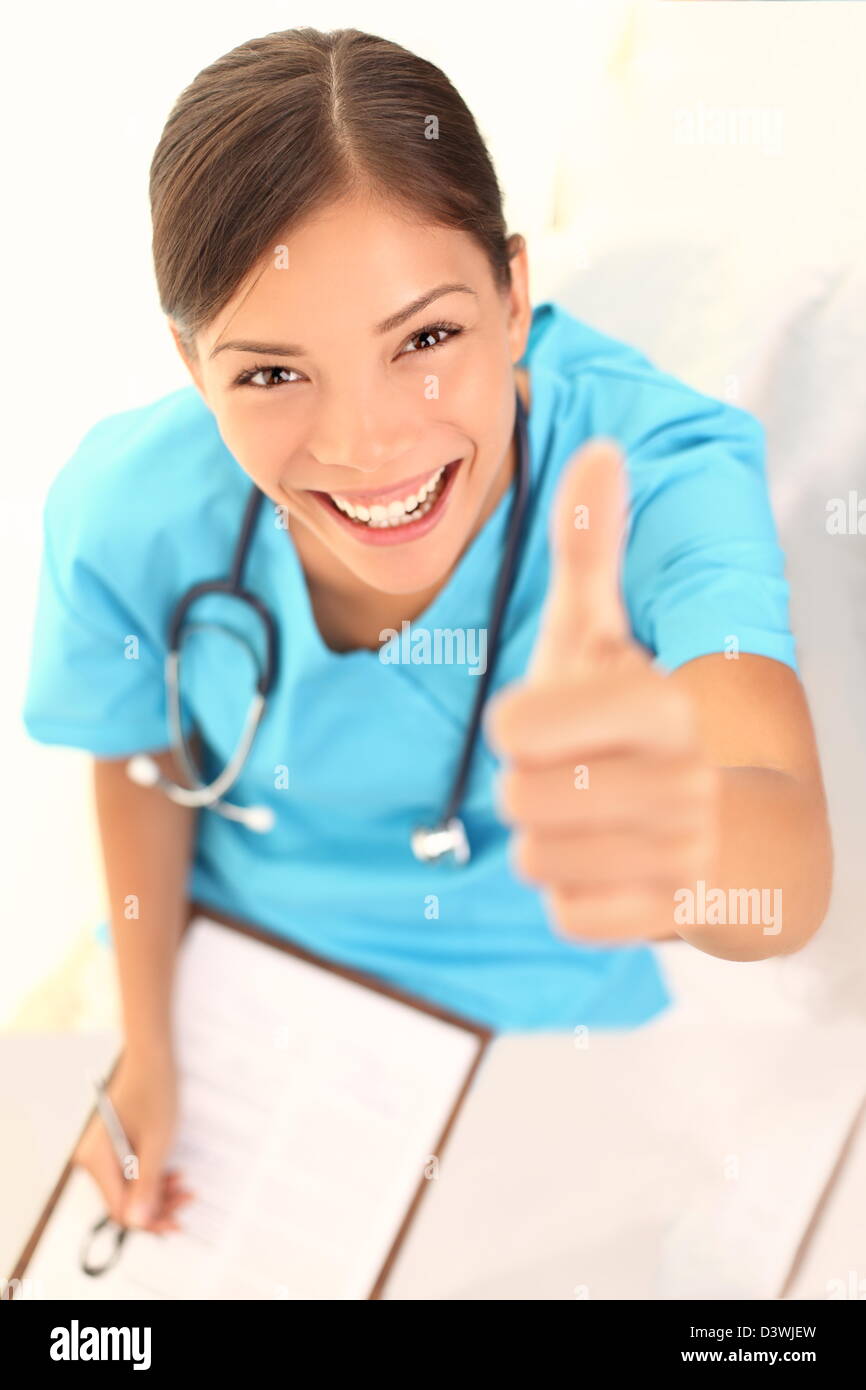 Portrait of smiling beautiful young female nurse or doctor with clipboard showing thumbs up sign Stock Photo