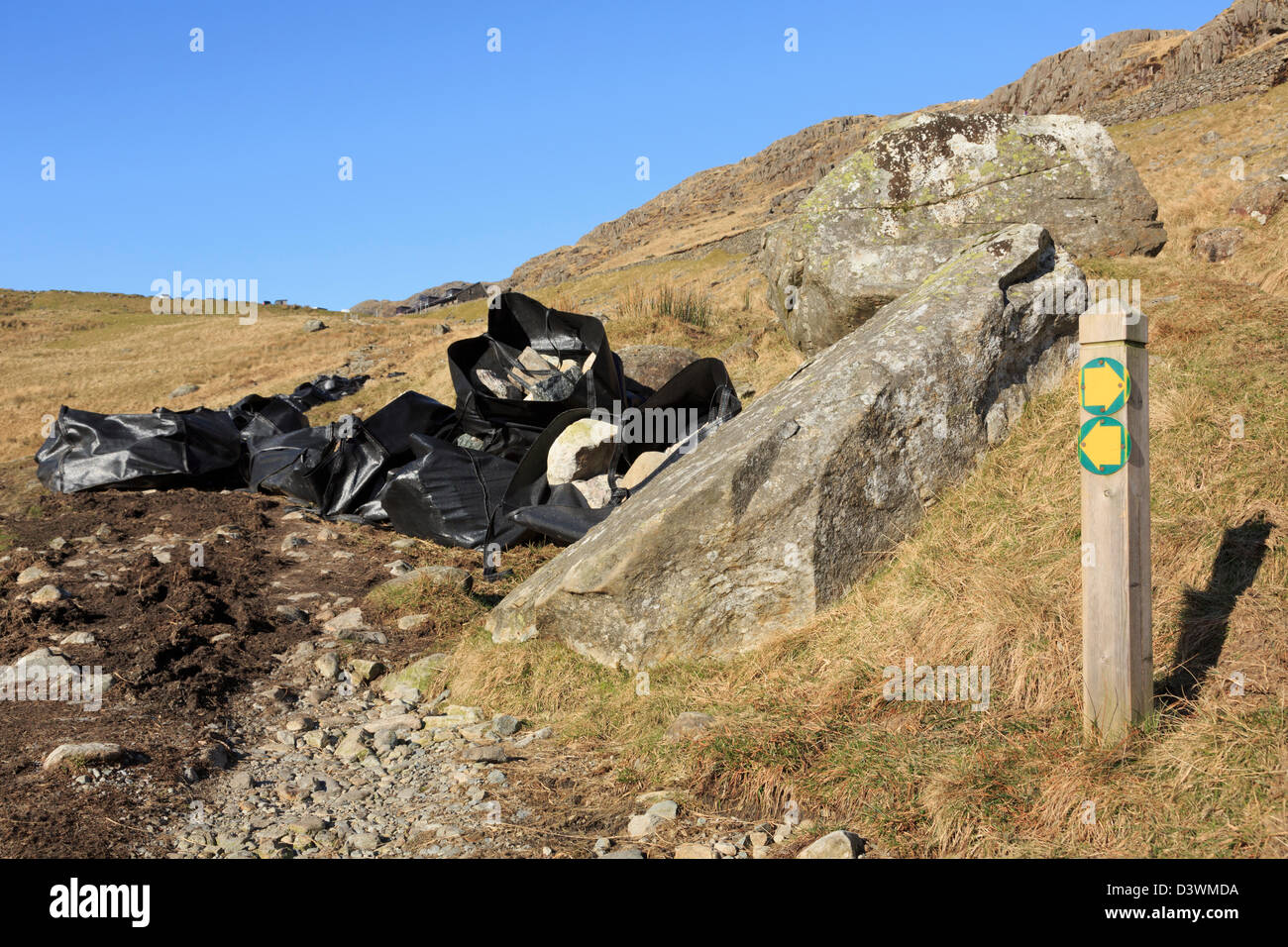 Bags of stones by waymarker sign on new footpath to Pen-y-Pass in Snowdonia National Park, Gwynedd, North Wales, UK Stock Photo