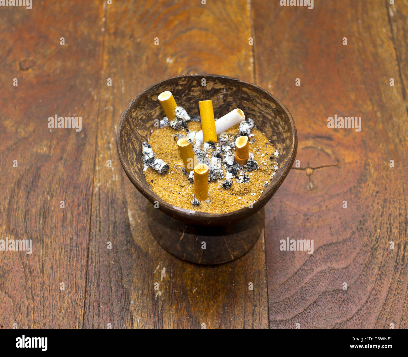 shell cigarettes CIGARETTES WITH ASH AND NICOTINE STAINS STUBBED INTO A SAND FILLED COCONUT  SHELL Stock Photo