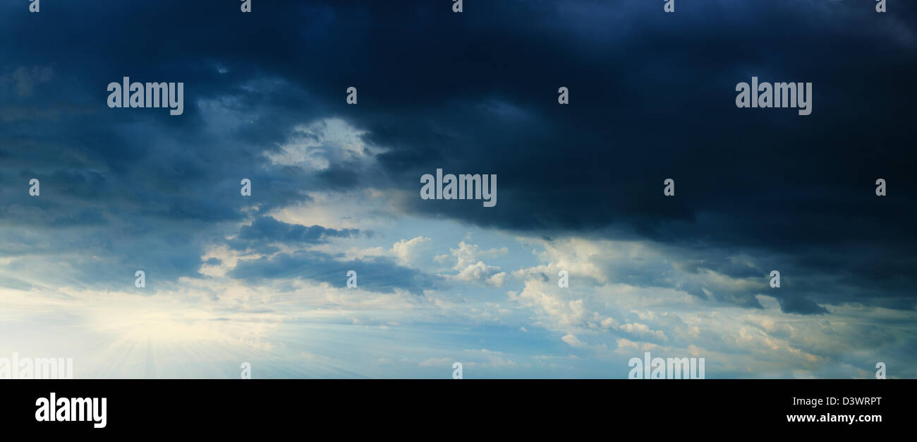 Sunbeams in stormy dark cloudy blue sky. Panorama from several photos. Stock Photo