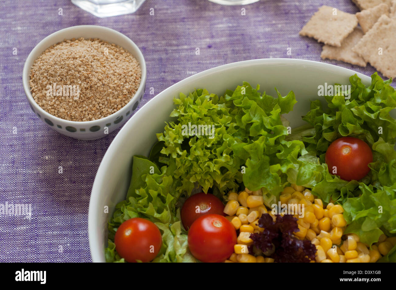 Close-up view of fresh organic mixed salad: lettuce, sweet corn, tomato. Gomasio condiment on the left Stock Photo