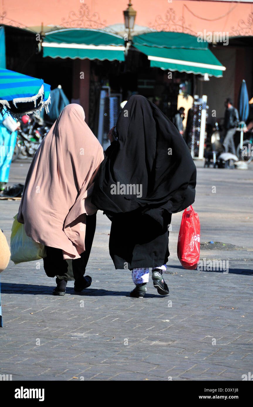 Two Moroccan women wearing the abaya or traditional dress for Arab women walking across the Jemaa El Fna plaza in Marrakech, Morocco Stock Photo