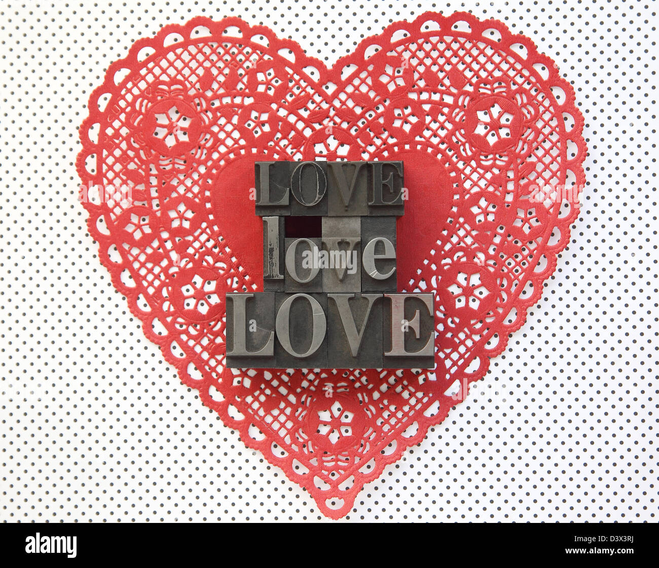 the word 'love' in old metal type on a Valentine doily against a polka dot background Stock Photo