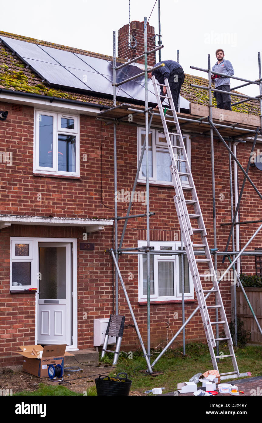 Two men fitting solar panels on the roof of a house in the Uk Stock