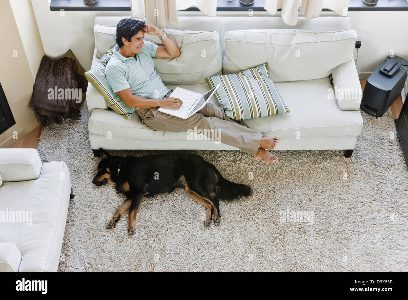 A young casual Mexican-American man surfing internet using laptop while relaxing at home Stock Photo