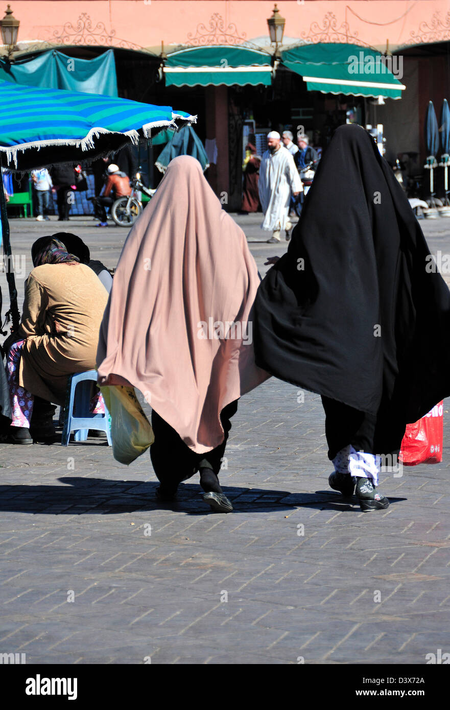 Two Moroccan women wearing the abaya or traditional dress for Arab women walking across the Jemaa El Fna plaza in Marrakech Stock Photo
