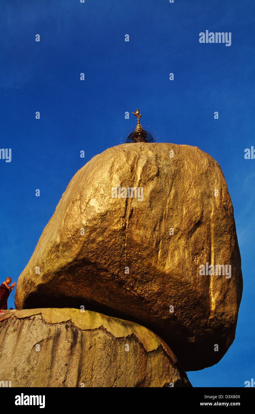 Monk praying by the goldleafed balancing boulder (Gold Rock) at sunset